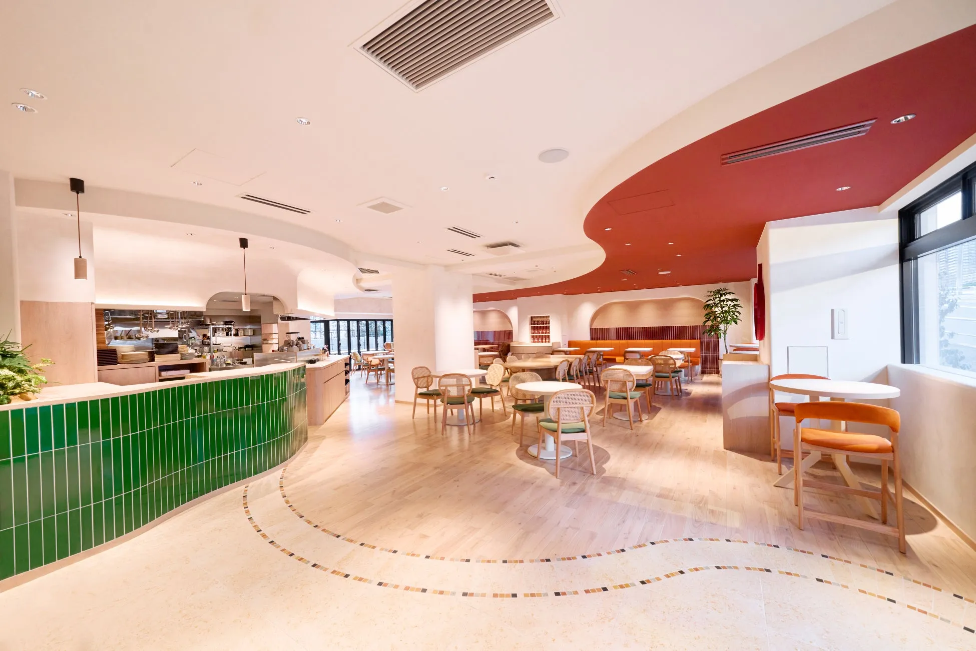 モダンなレストランのインテリア。緑のタイル張りのカウンター、木製の床、丸いテーブルと椅子が配置され、赤い天井がアクセントになっています。