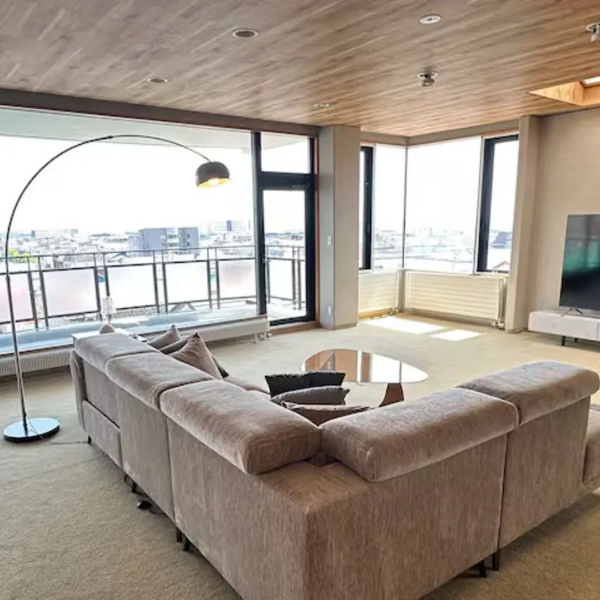 広々としたモダンなリビングルームで、大きなL字型ソファと曲線的なフロアランプが特徴です。