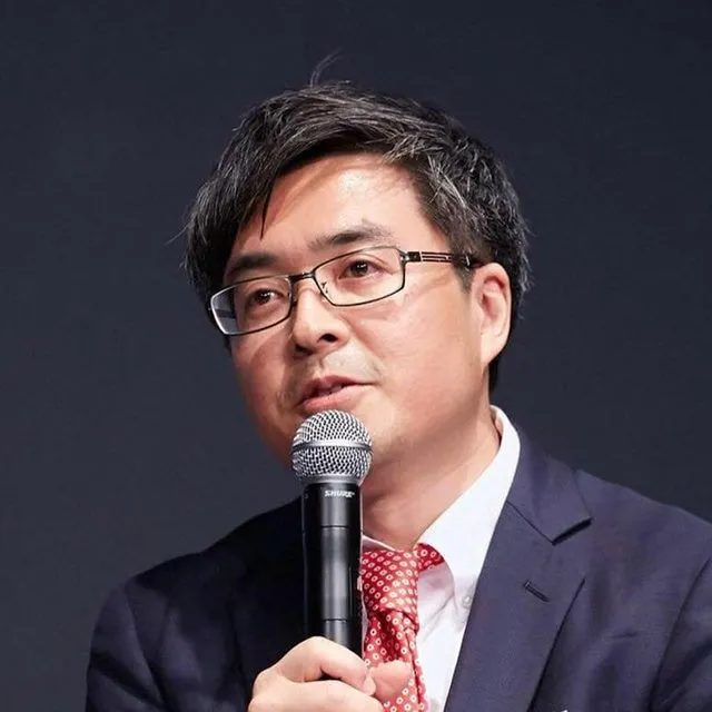 眼鏡をかけた男性がマイクを持って話している様子