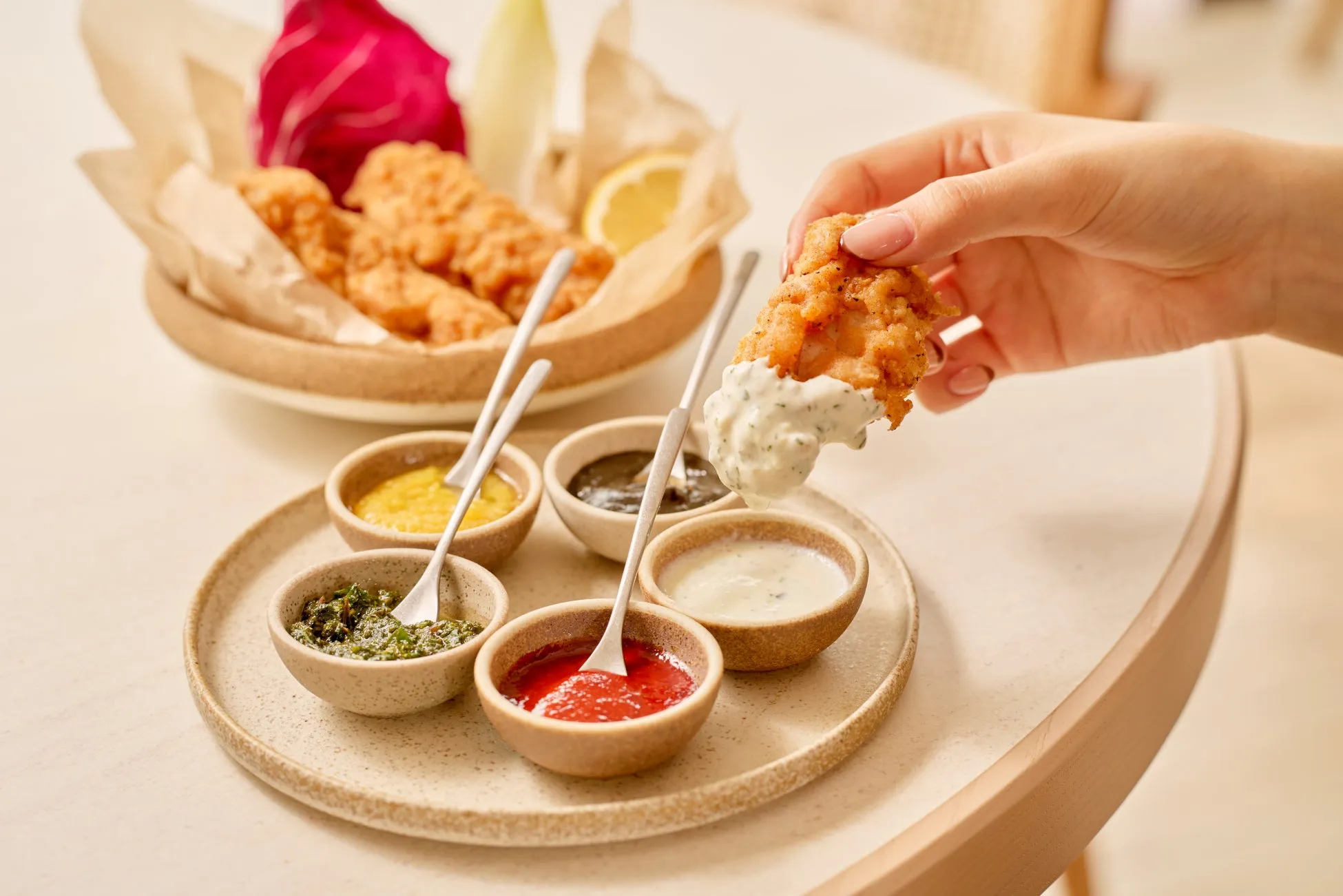 揚げ物料理と様々なソースの画像。女性の手が揚げ物をソースにつけている様子が写っています。周りには様々なソースが入った小さな器が並んでおり、美味しそうな印象を与えます。