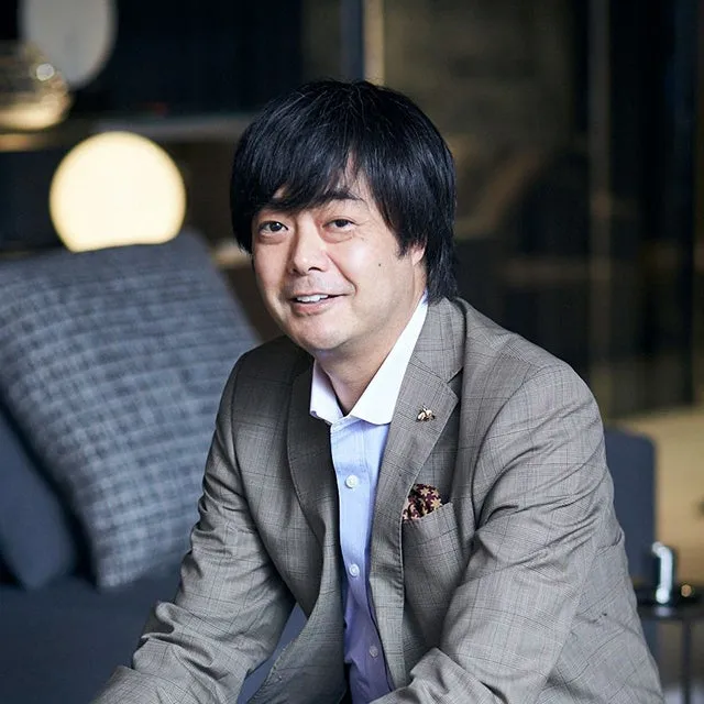 ジャケット姿の男性が笑顔でカメラを見つめている写真。