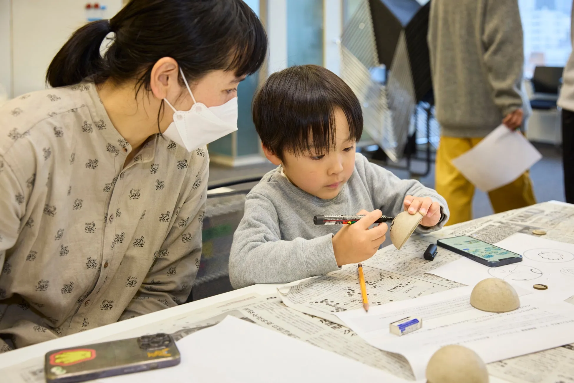 子供が工作をしている様子。マスクをした女性がそばで見守っている。