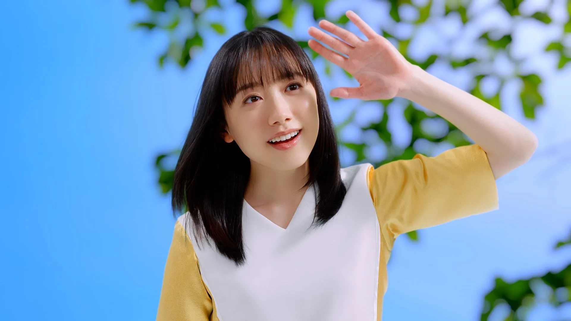 青空の下、女性が日差しを避けるように手をかざしている様子