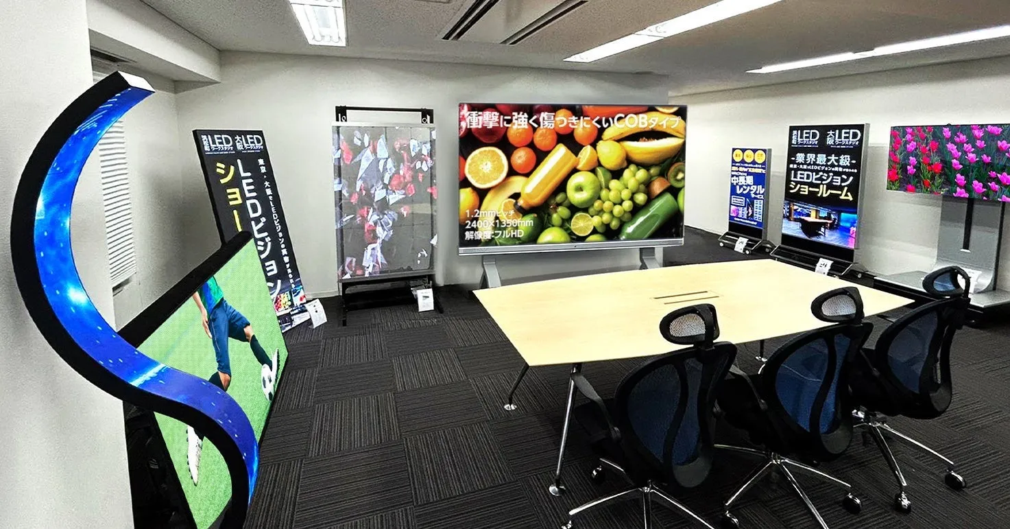 LEDディスプレイのショールームで、様々な製品が展示されている。大型スクリーンにはフルーツやサッカー、花などの鮮やかな映像が映し出され、曲面型ディスプレイも目を引く。製品説明やレンタル情報も掲示されている。