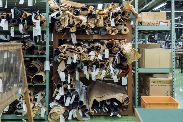 革製品の製造工場と思われる場所の写真。棚に革のロールがぎっしりと並べられ、タグが付けられている。奥には作業スペースが見える。