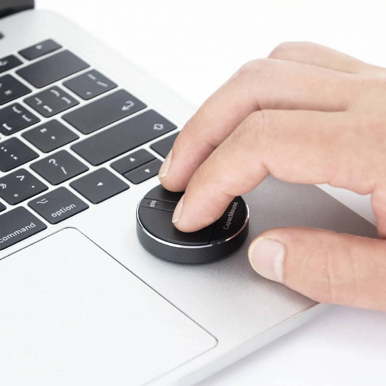 MacBookのトラックパッド上に置かれたCapaMouseを操作している手のクローズアップ画像です。CapaMouseは、黒い円形のデバイスで、人差し指で操作しています。