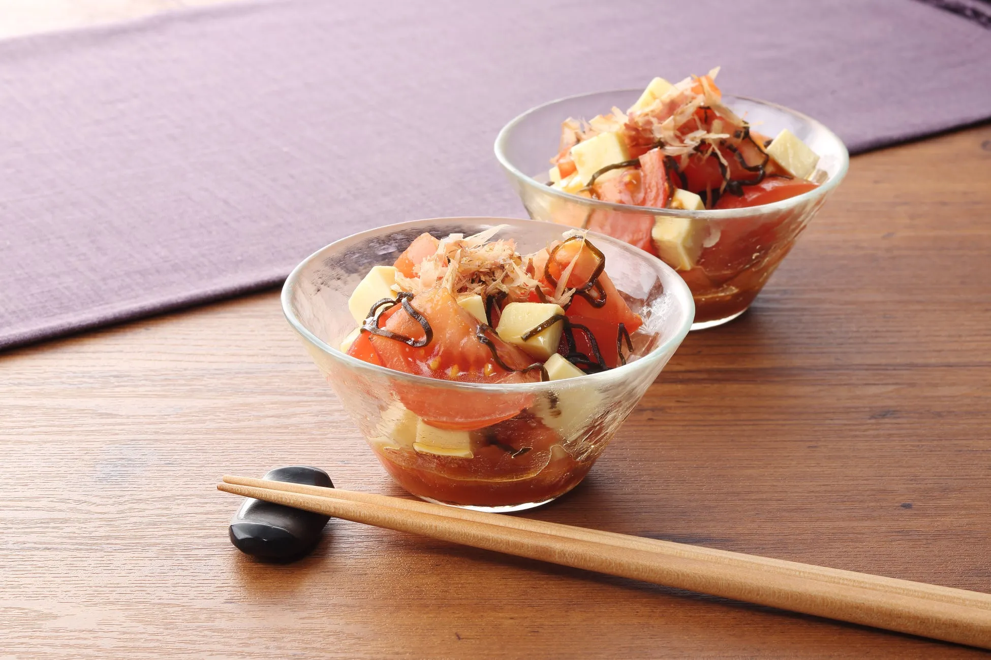 2つのガラスのボウルに入った、トマト、豆腐、鰹節、海苔を使った料理が写っています。箸と箸置きも写っています。