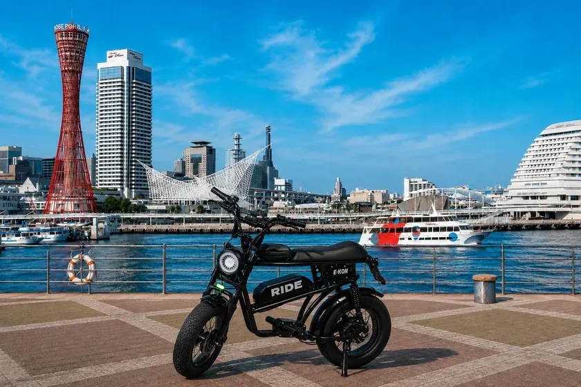神戸のハーバーランドに停まっている電動バイクの写真です。赤いポートタワーや周囲の建物が写っており、青い空と海が背景に広がっています。