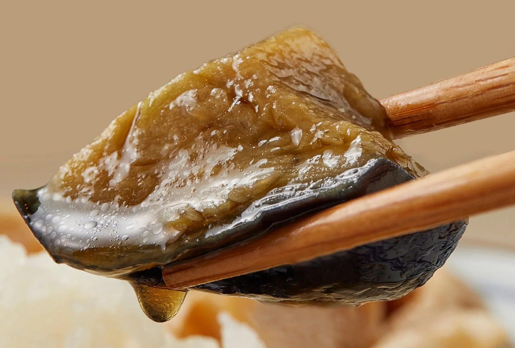 箸で持たれた、照りのある茄子の煮物。滴が落ちている。