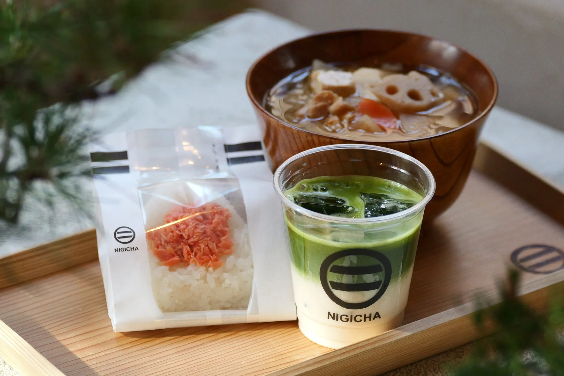 おにぎり、味噌汁、抹茶ラテが木製のトレーに載せられた食事の画像
