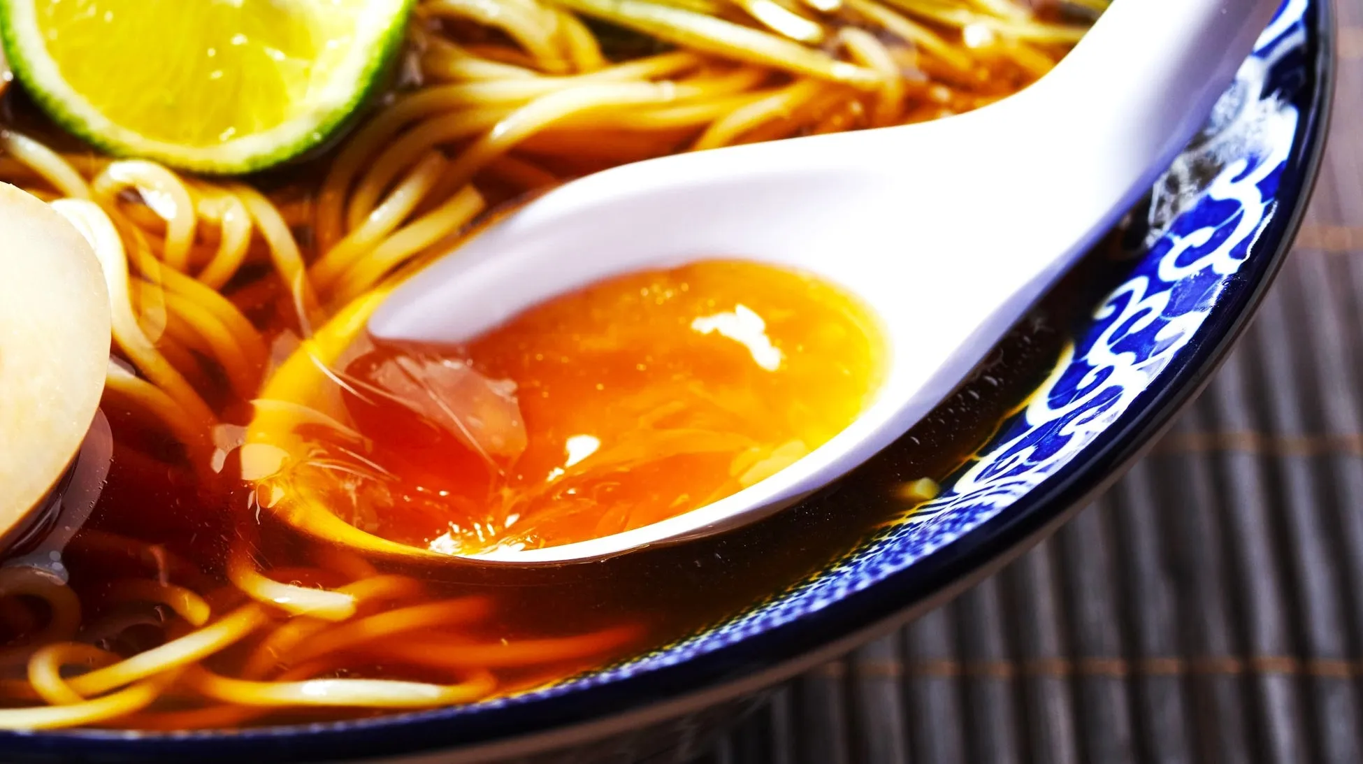 ラーメンのクローズアップ画像で、とろりとした半熟卵の黄身がスプーンに乗せられています。