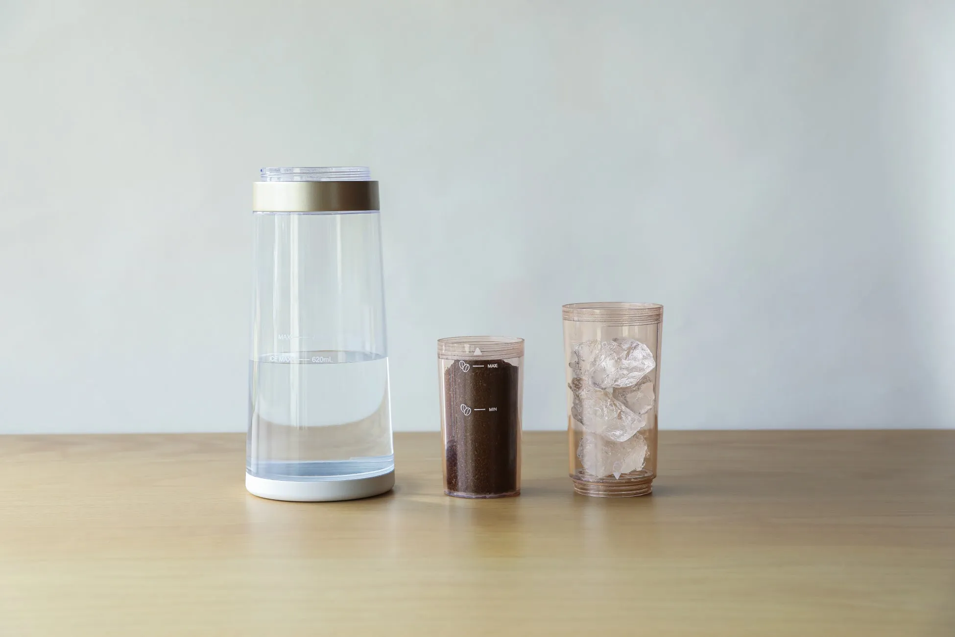 木製のテーブルの上に、水が入った透明なピッチャー、挽いたコーヒー豆が入った容器、そして氷が入ったグラスが並べられています。水出しコーヒーを作る準備をしている様子が伺えます。